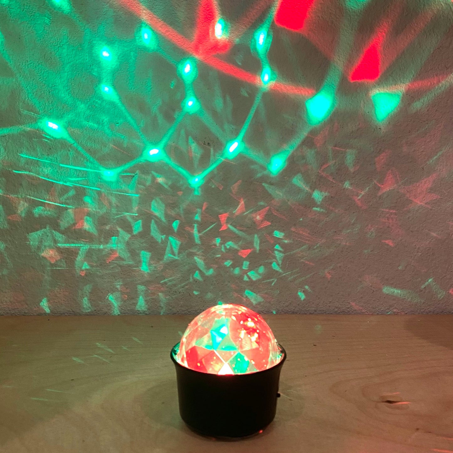 Colorful disco ball with red and green lights on a wooden floor.