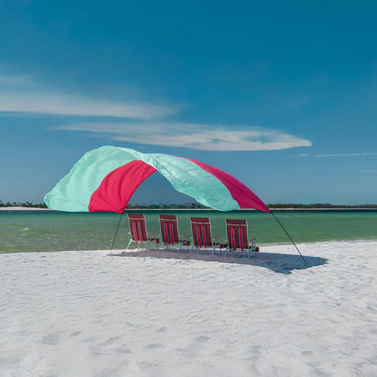 Mint and berry colored beach shade with mint and berry colored chairs underneath on a sandy beach.