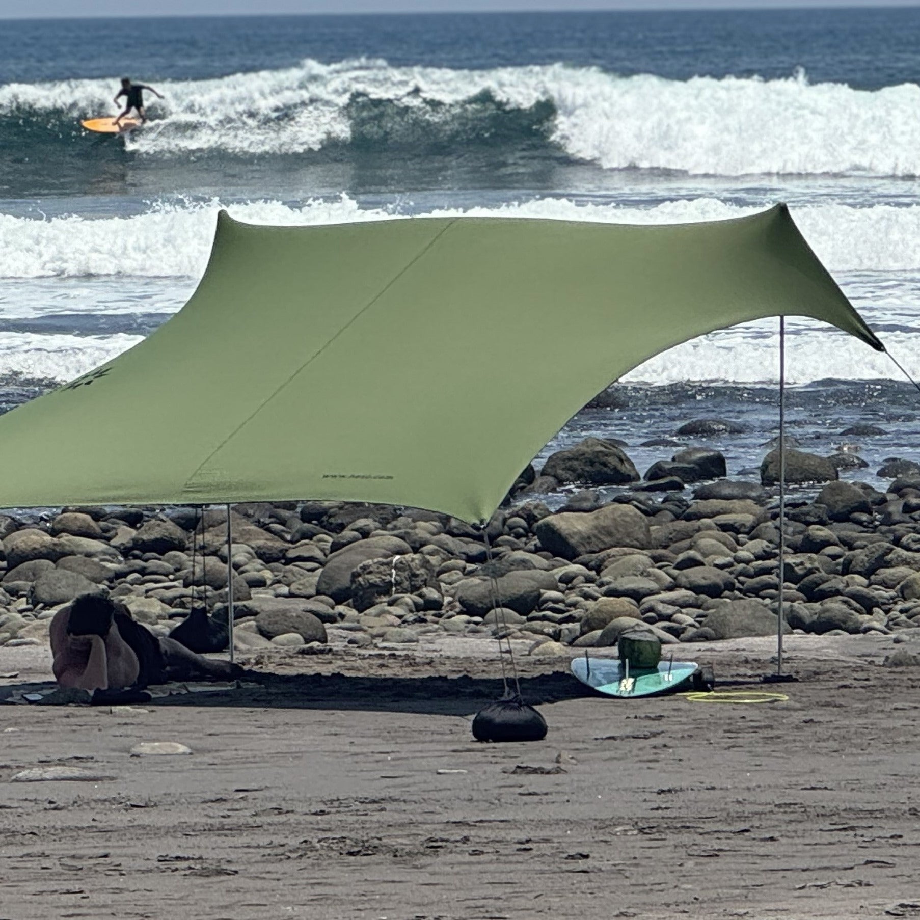 Green canopy set up on a rocky beach with ocean waves in the background