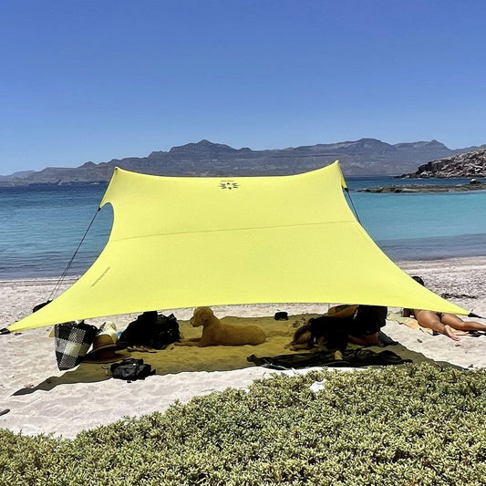 Yellow tent set up on a beach with ocean and mountains in the background