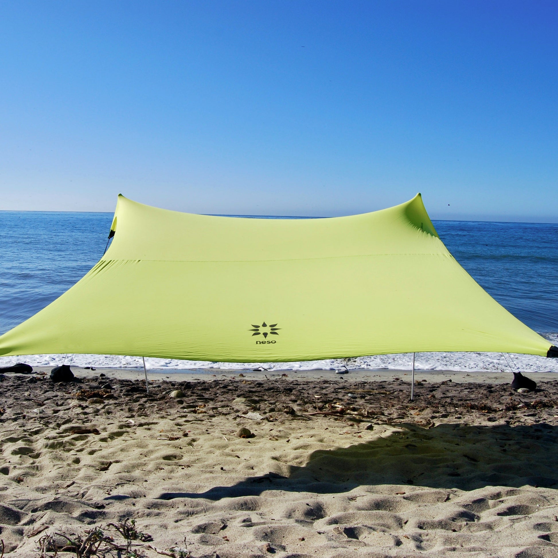 Lemon yellow NESO tent set up on a sandy beach with ocean and clear blue sky in the background