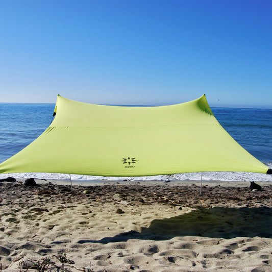 Lemon yellow NESO tent set up on a sandy beach with ocean and clear blue sky in the background