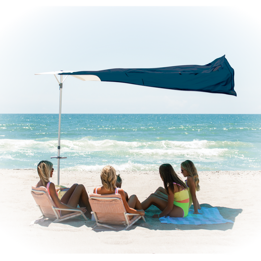 Four people sitting on beach chairs under a large navy colored beach shade with ocean view.