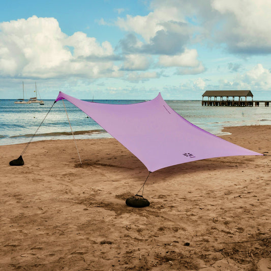 Purple NESO beach canopy on a sandy beach with ocean and pier in the background
