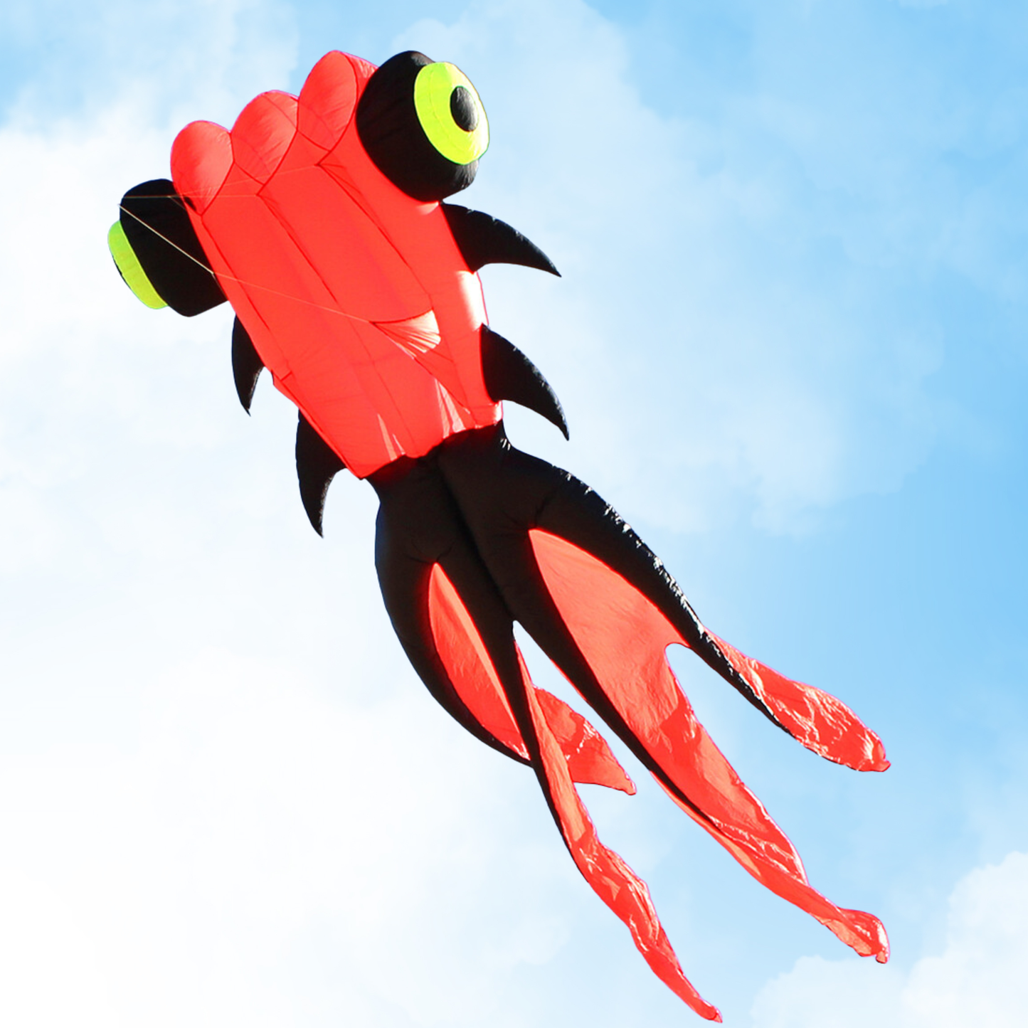 Red and black goldfish kite with green eyes against a blue sky