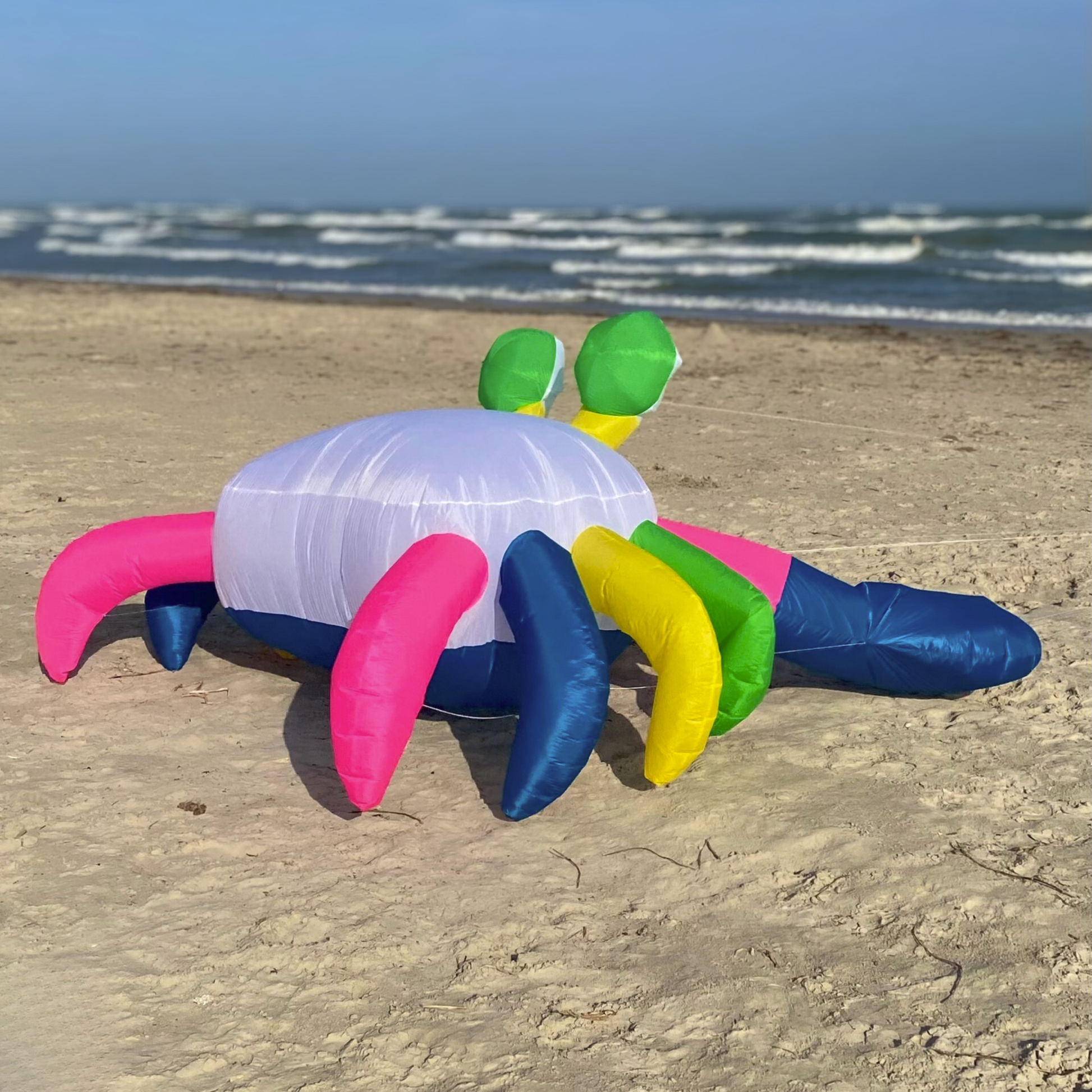 Colorful inflatable crab kite on a sandy beach with ocean in the background