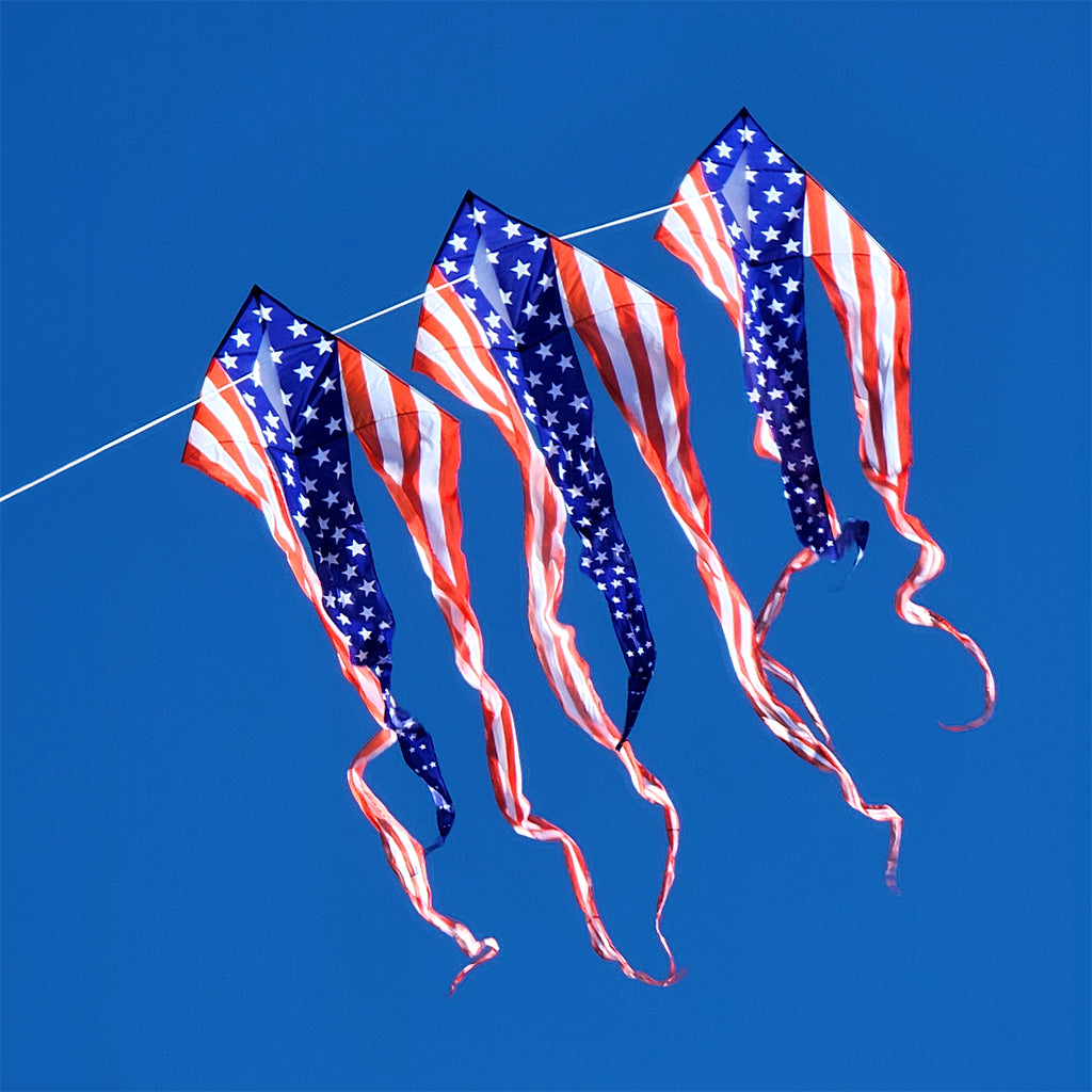 Three American flag kites against a clear blue sky