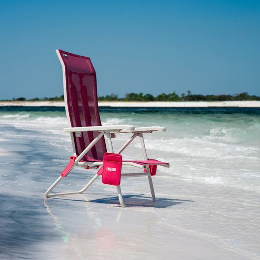Pink beach chair on a sandy beach with clear blue water and sky.