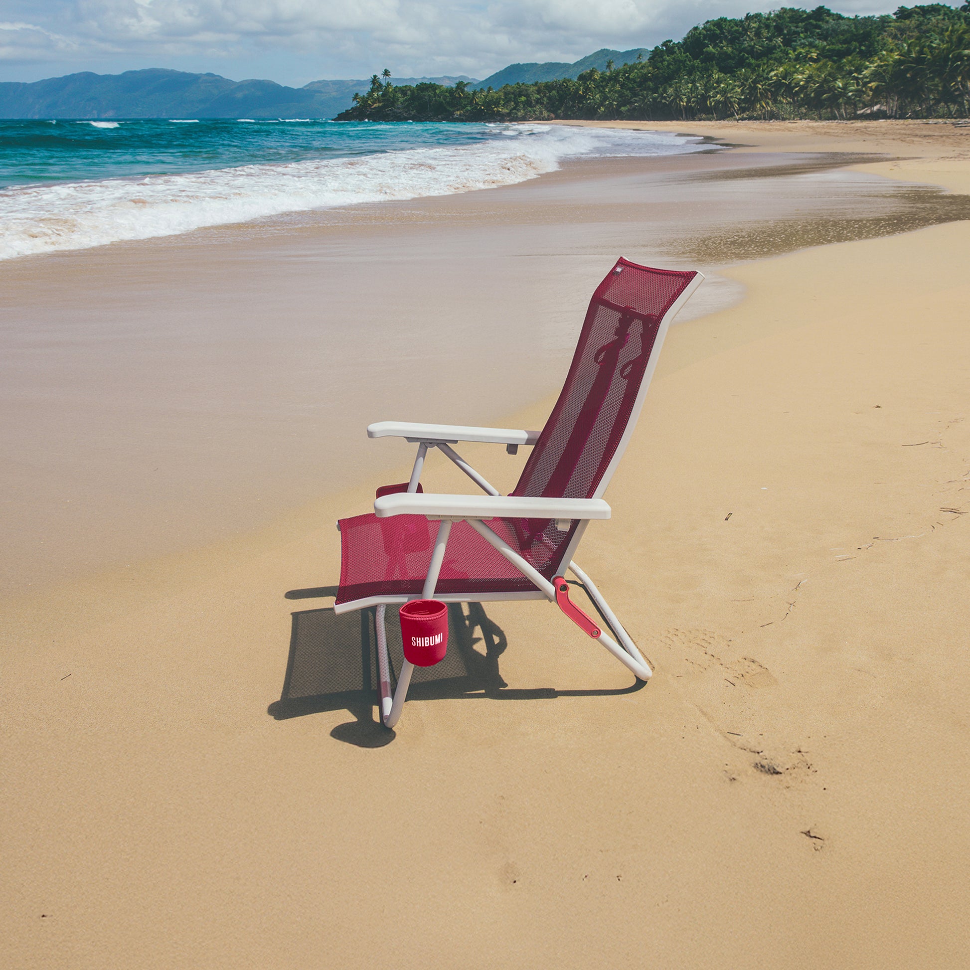 Pink and white beach chair on a sandy beach with ocean and mountains in the background