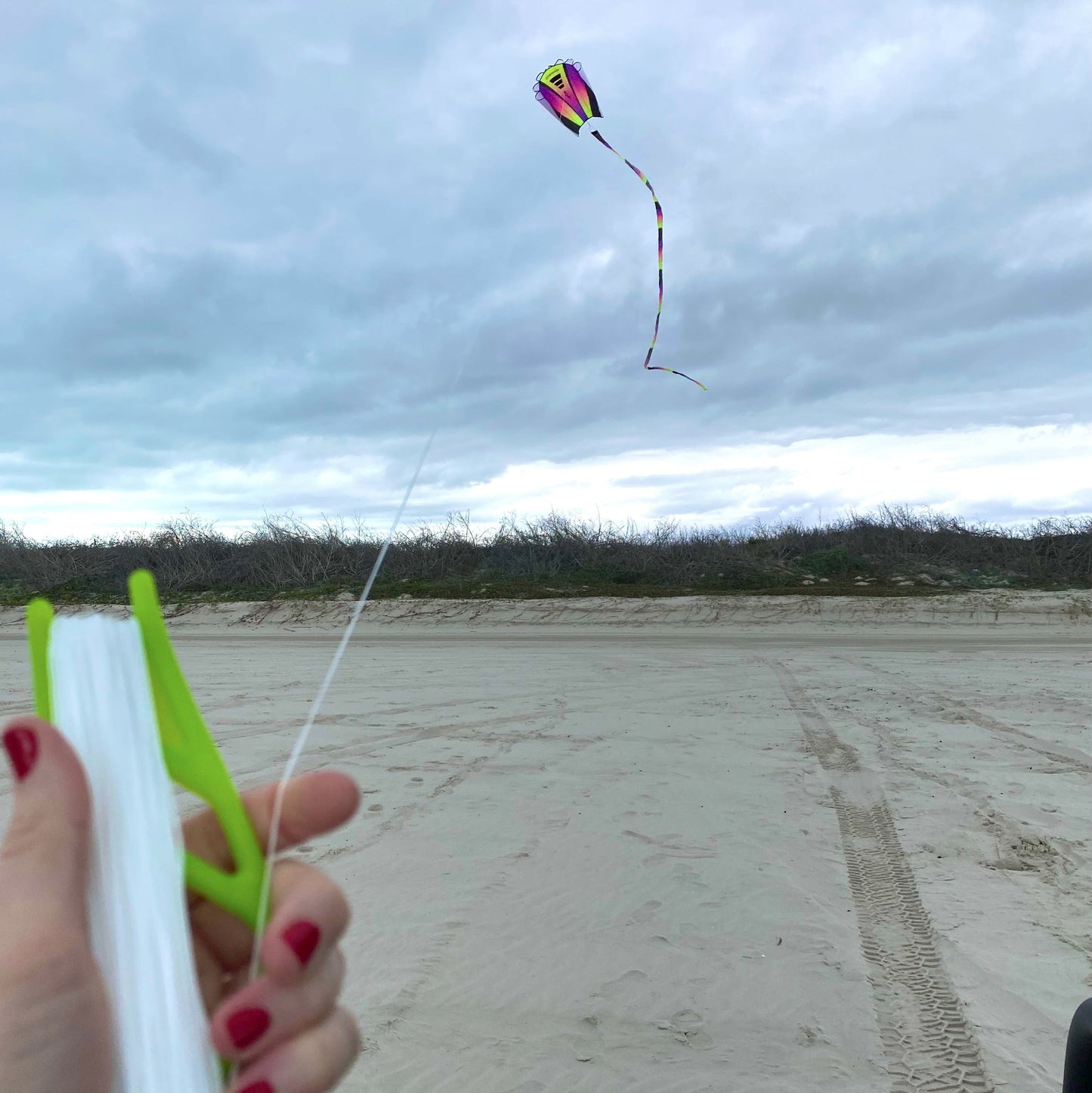 Person holding a green handle with kite string, flying a colorful kite against a cloudy sky.