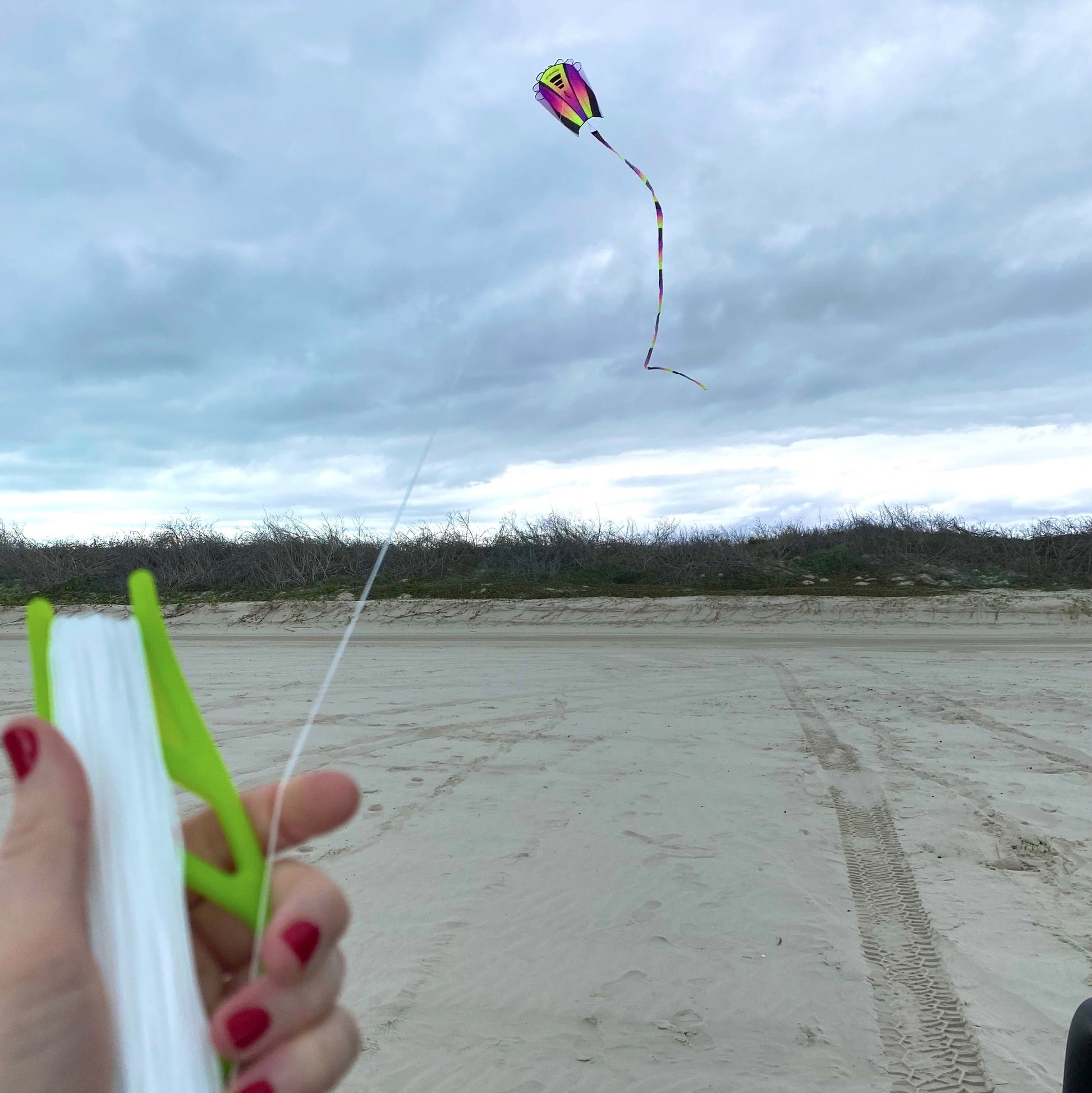 Person holding a green handle with kite string, flying a colorful kite against a cloudy sky.
