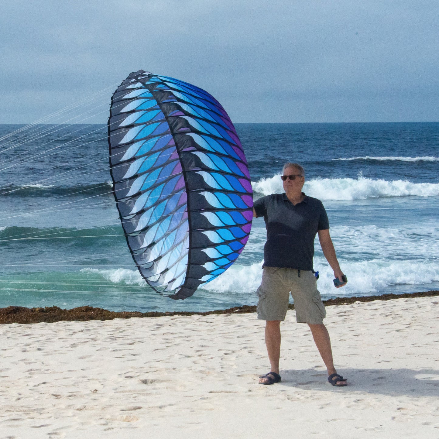 Person standing next to a blue and purple bol on a beach with ocean waves in the background