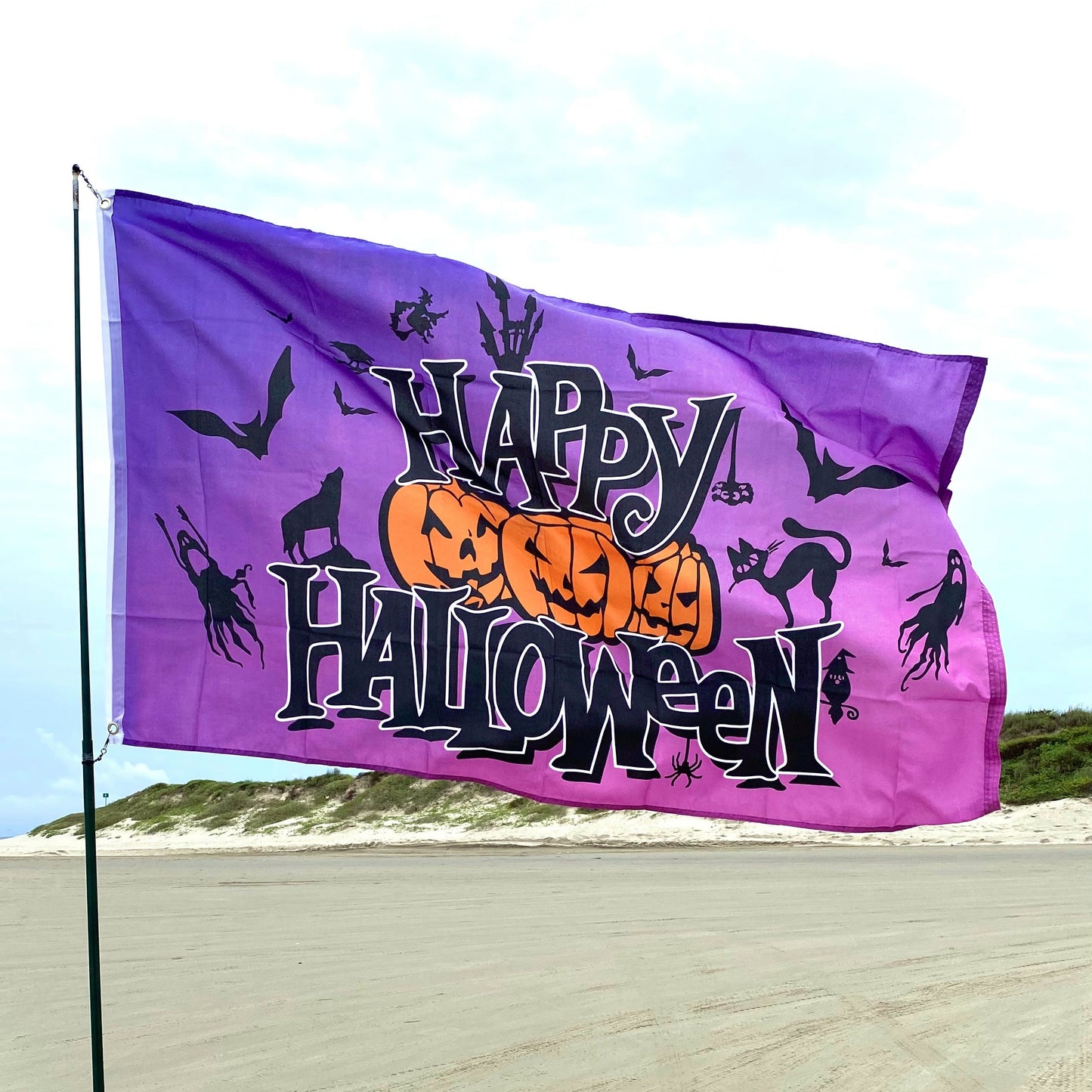 Halloween-themed flag with pumpkins, cats, and bats on a beach.