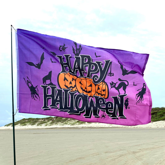 Halloween-themed flag with pumpkins, cats, and bats on a beach.