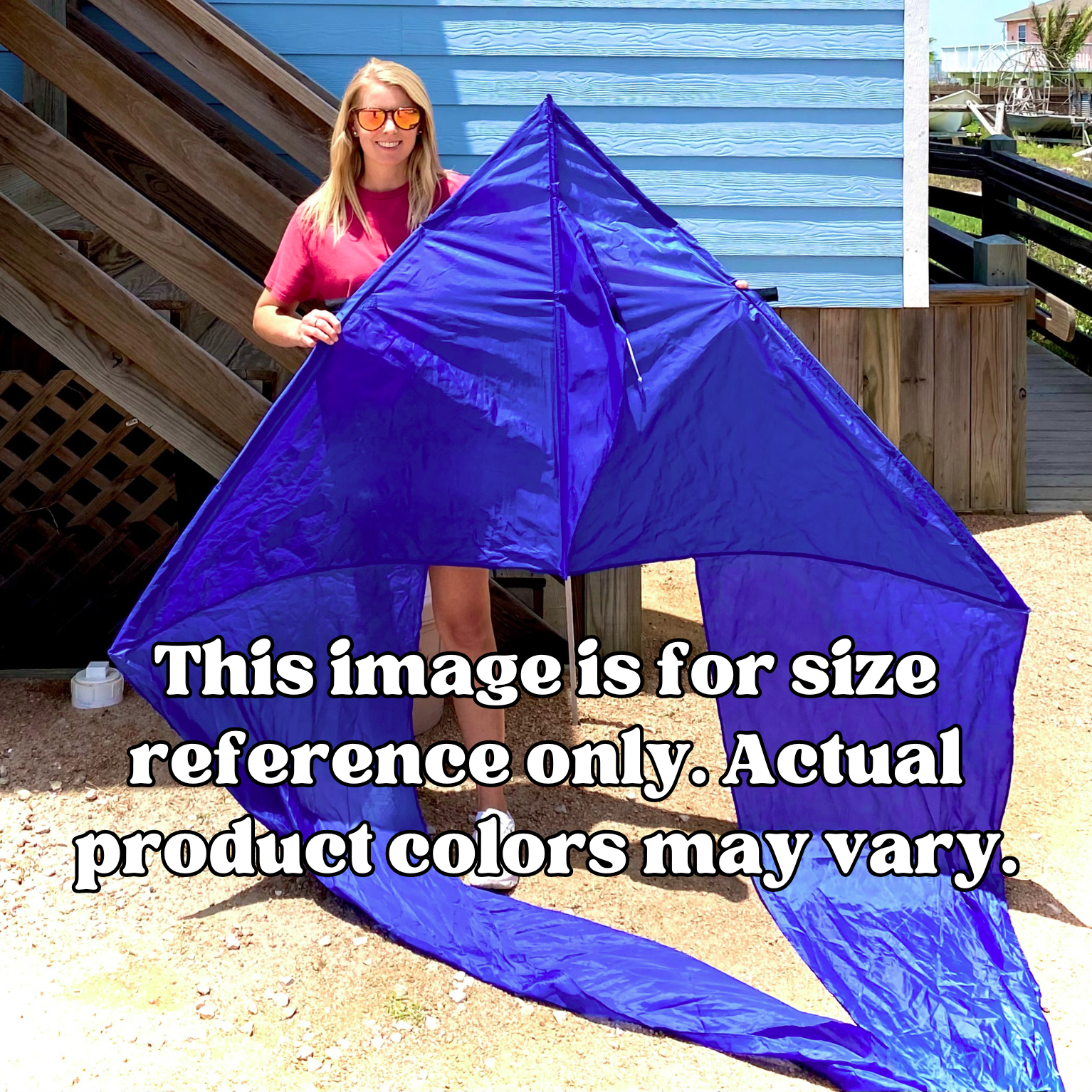 Woman holding a large blue kite with text overlay for size reference, American flag and house in background.