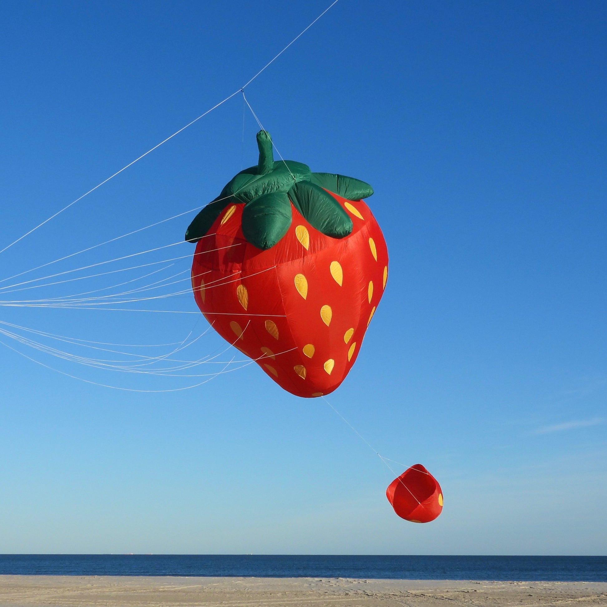 Strawberry-shaped kite flying against a clear blue sky with ocean in the background