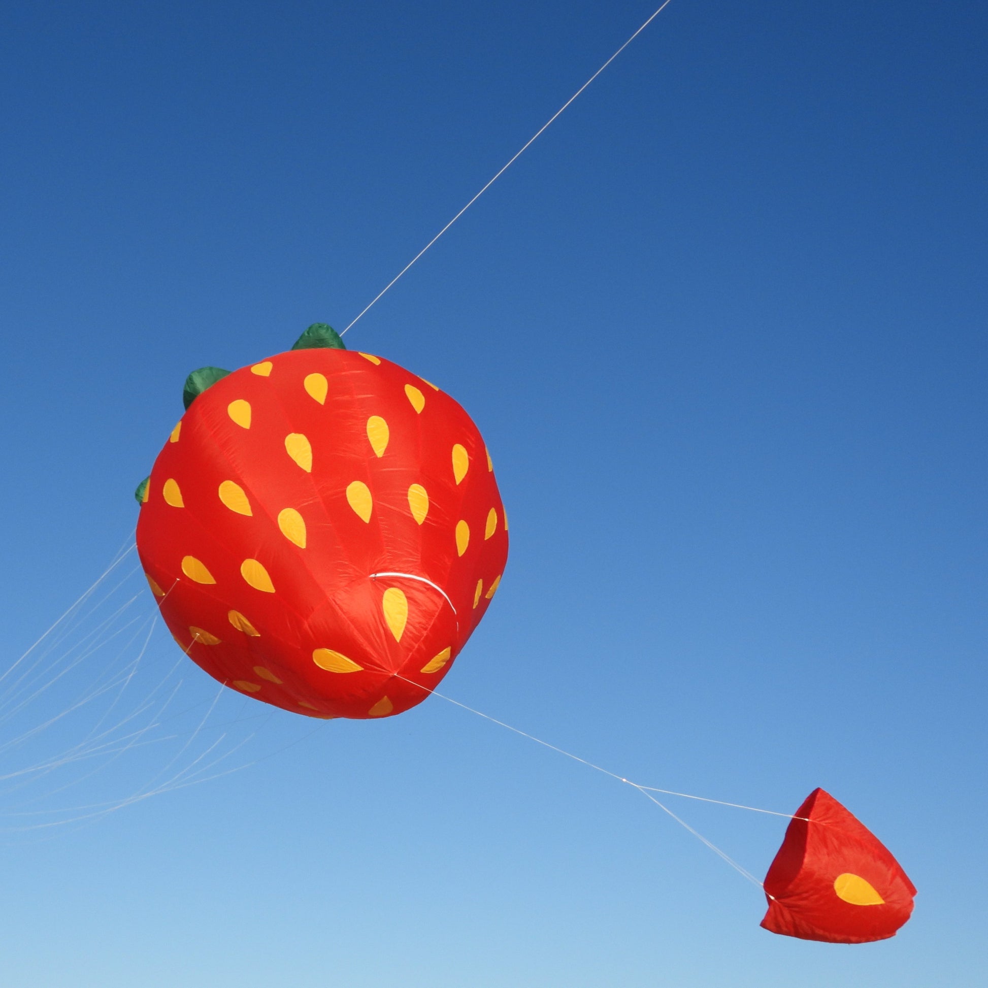 Strawberry-shaped kite against a clear blue sky