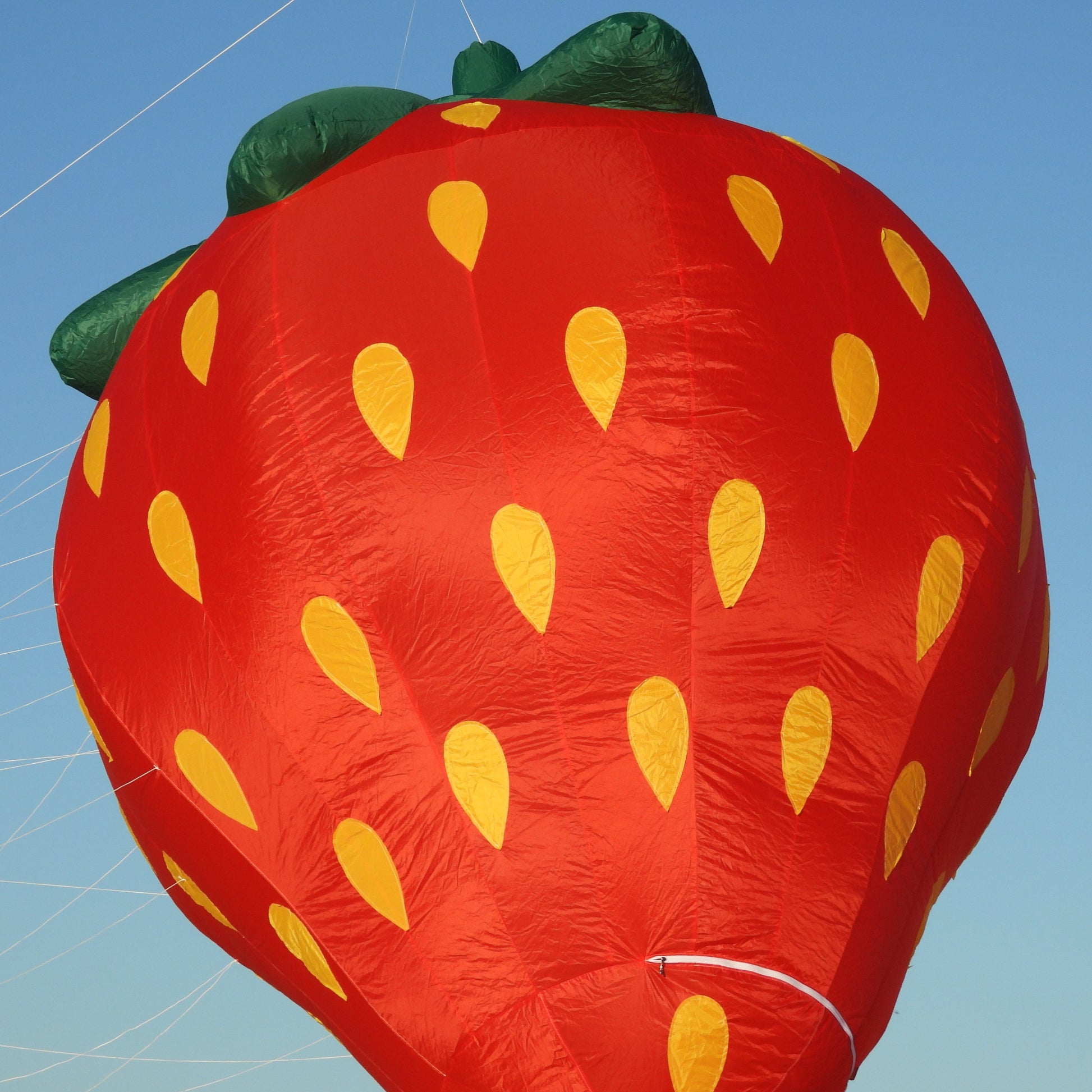 Inflatable strawberry-shaped kite against a clear blue sky
