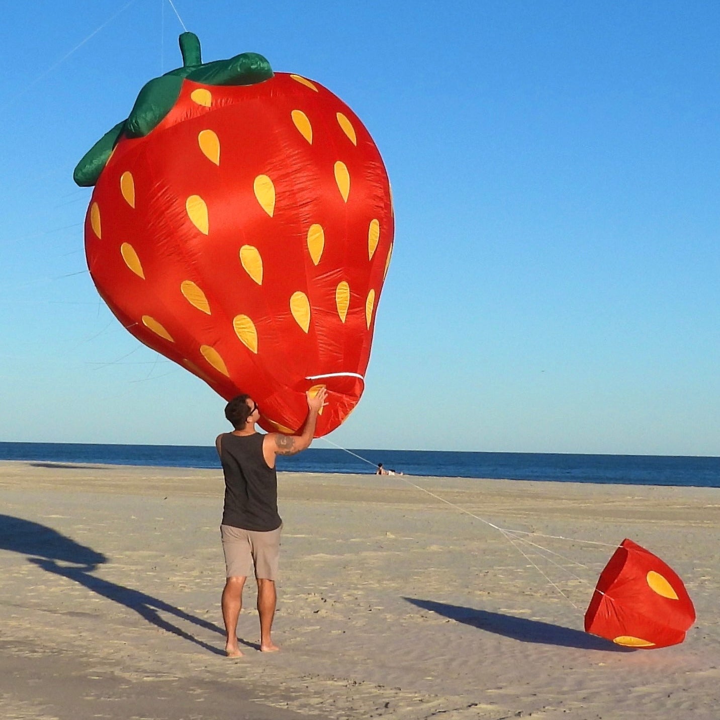 Person holding a large strawberry-shaped kite on a beach