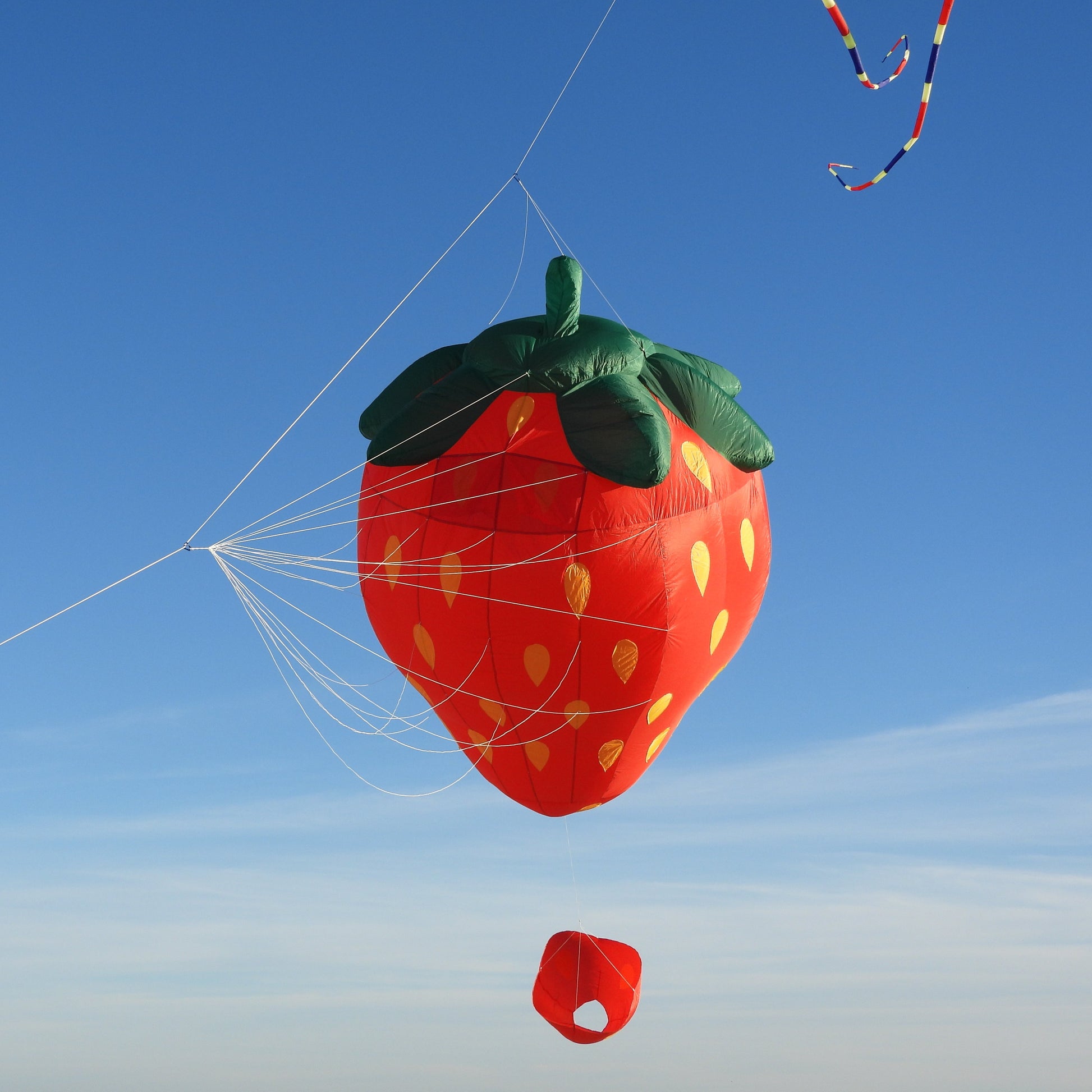 Strawberry-shaped kite flying against a blue sky