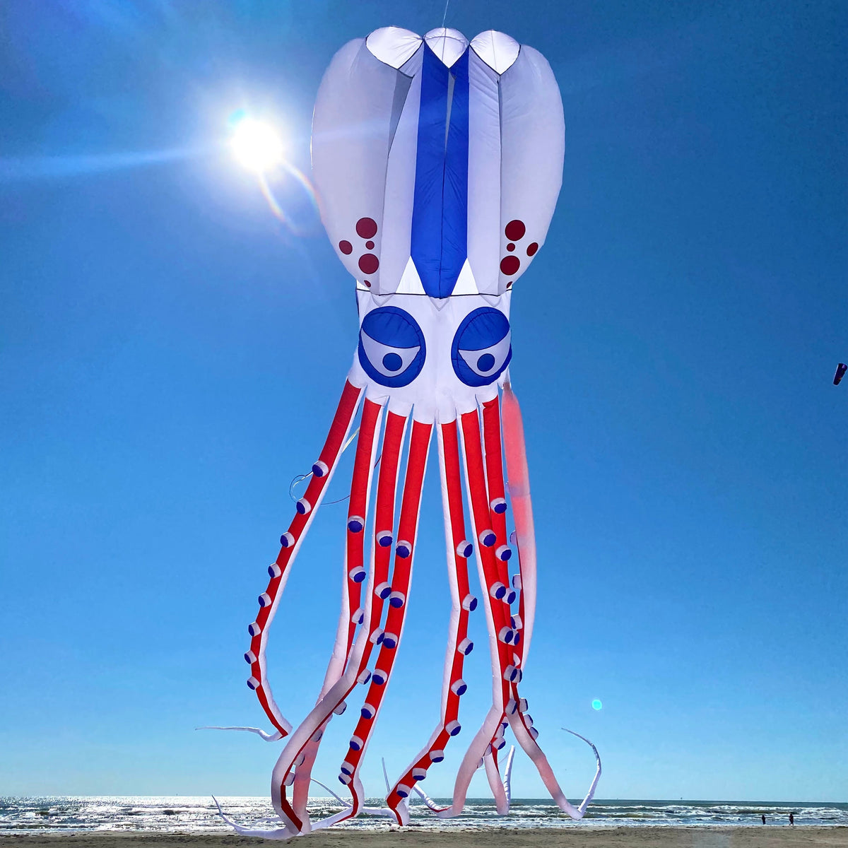 Red white an blue octopus-shaped kite on a beach with a clear blue sky.
