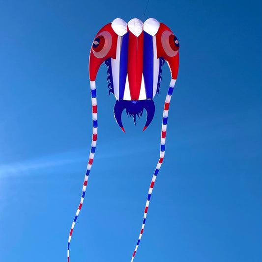 Red, white, and blue kite shaped like a trilobite against a clear blue sky