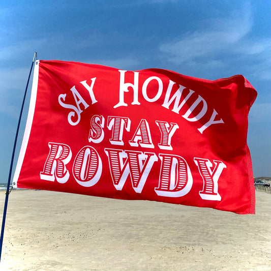 Red flag with 'SAY HOWDY STAY ROWDY' text on a beach