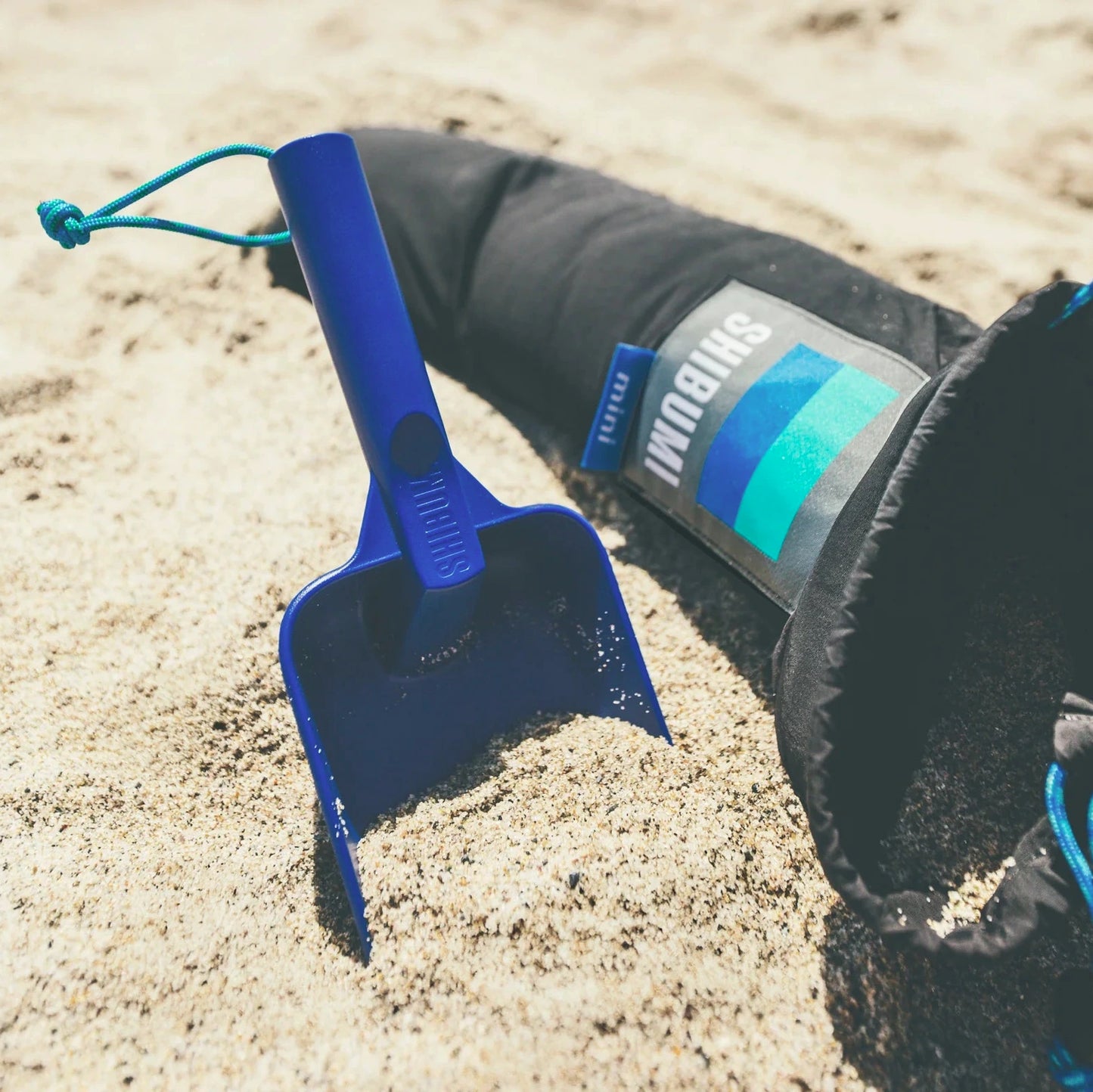 Blue sand shovel with a brand logo on a sandy surface