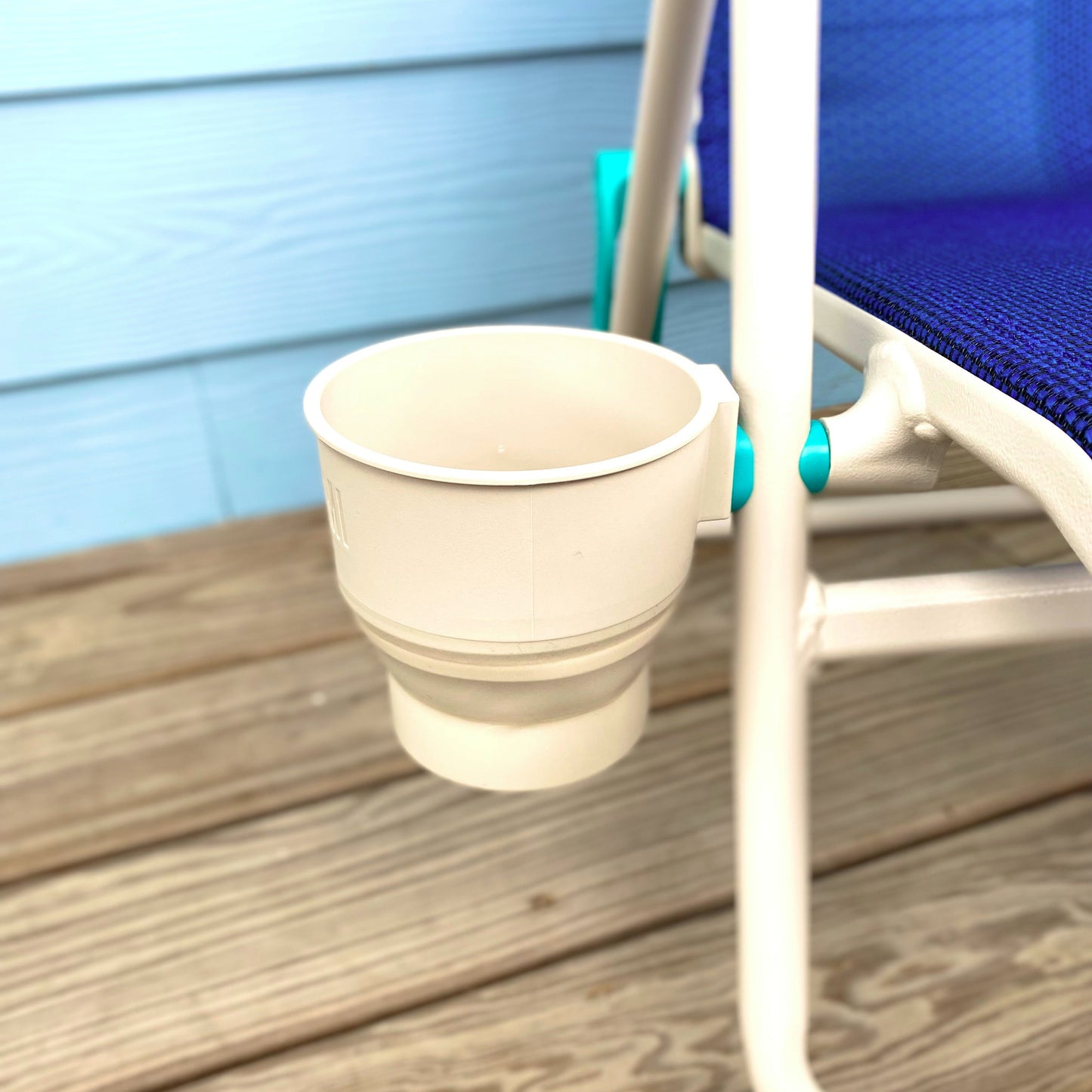 Collapsible beige cup holder on a wooden deck next to a blue chair