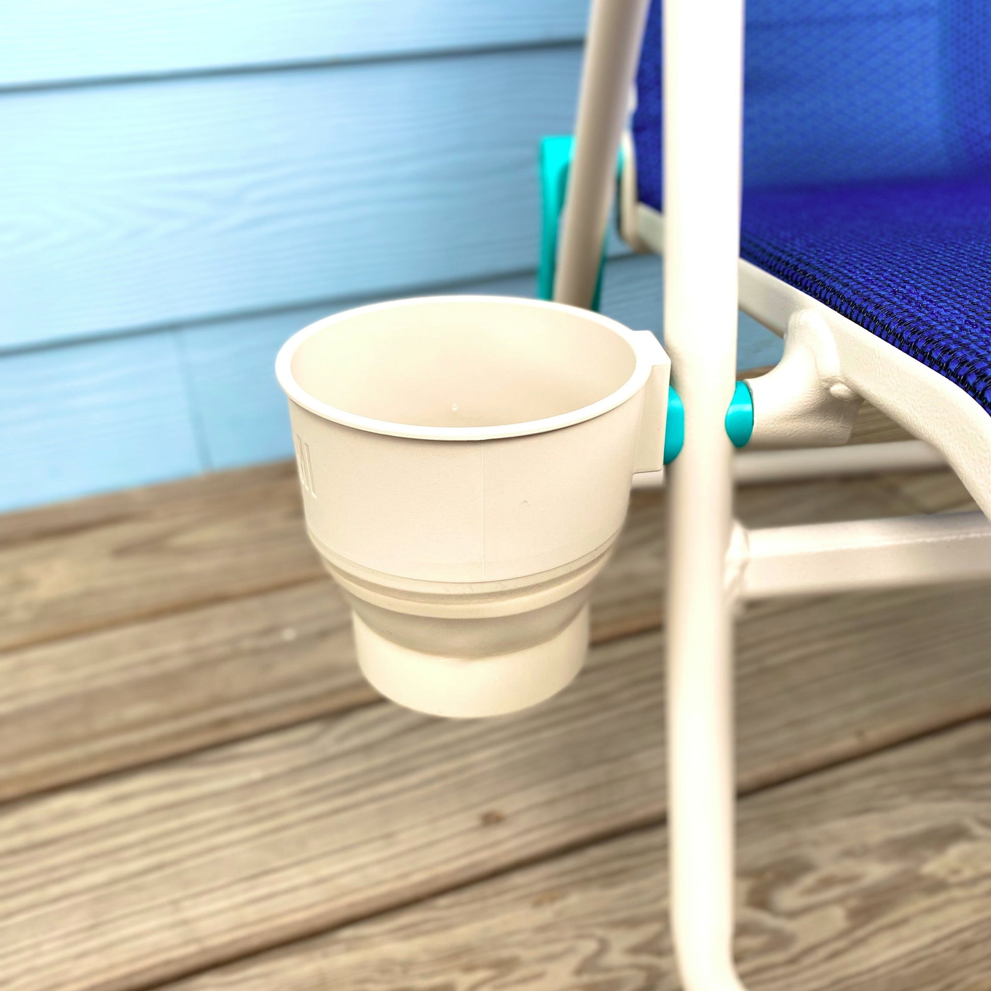 Collapsible beige cup holder on a wooden deck next to a blue chair