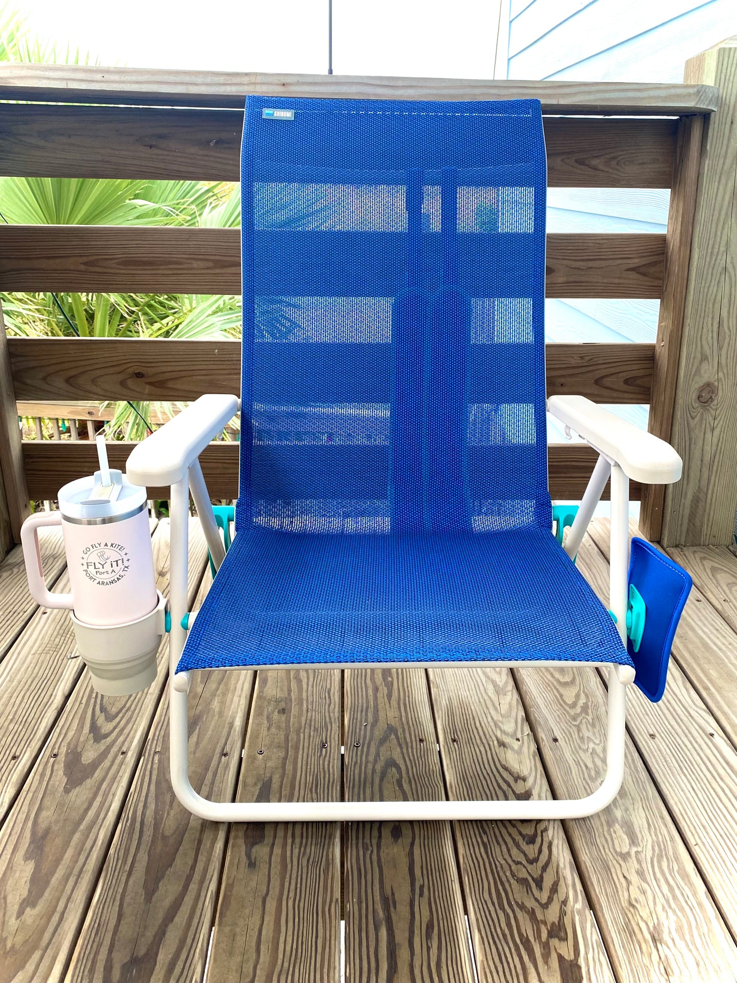Blue lounge chair on a wooden deck with a cup and straw in the background.