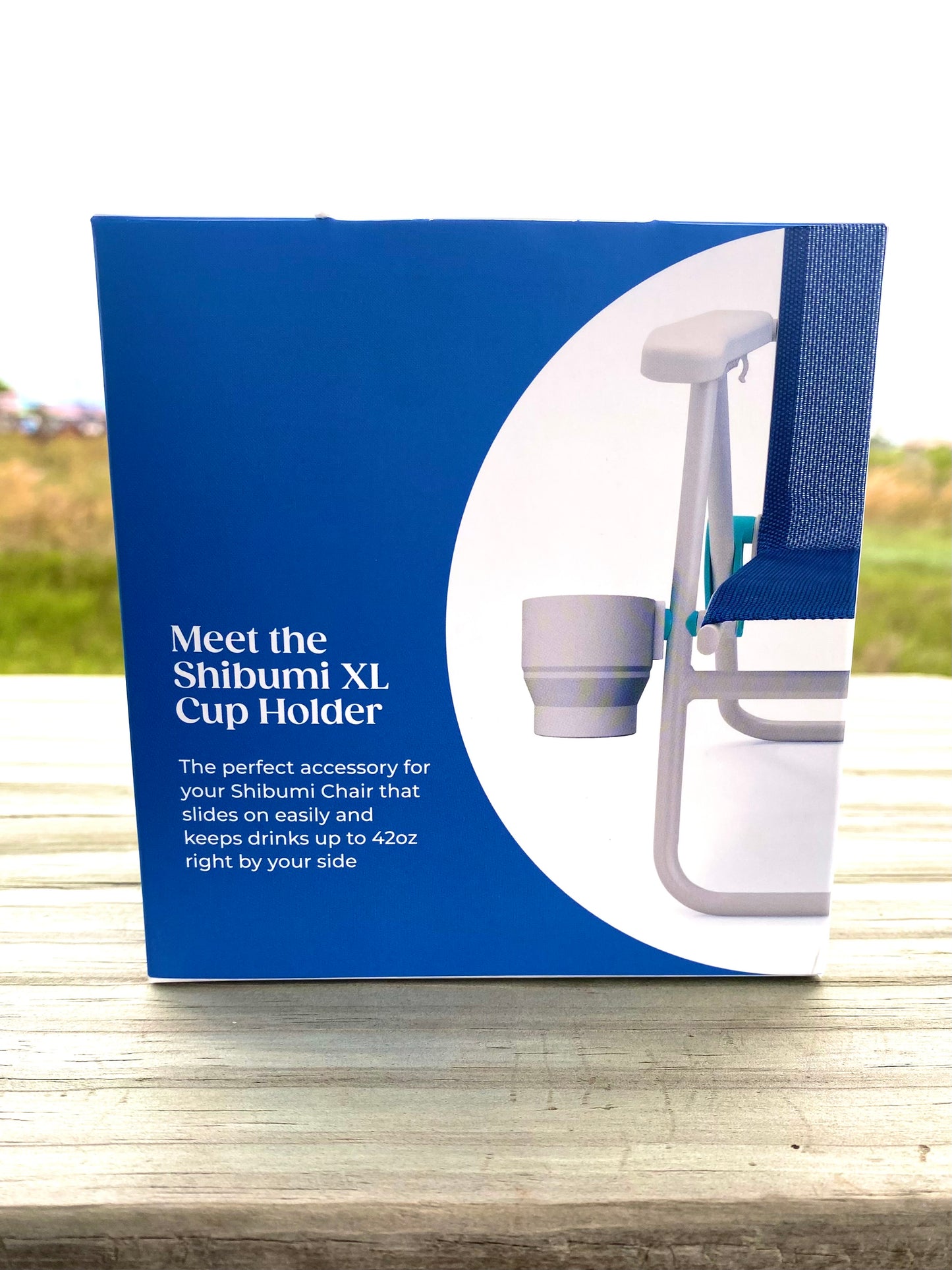 Shibumi XL Cup Holder packaging on a wooden surface with a blurred outdoor background