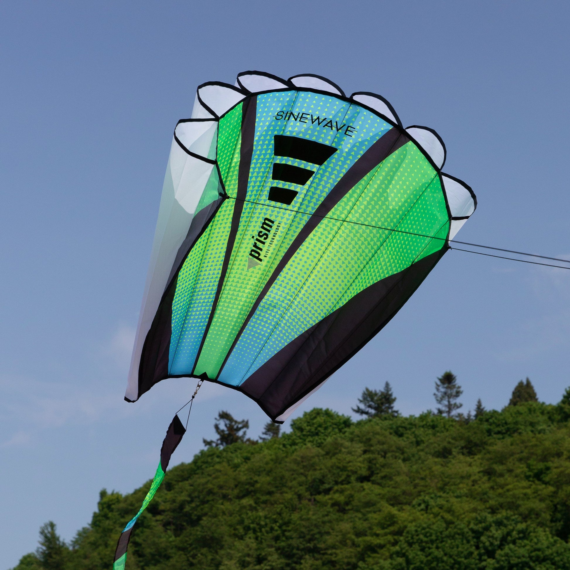 Green and black kite with 'SineWave' branding against a blue sky with trees below