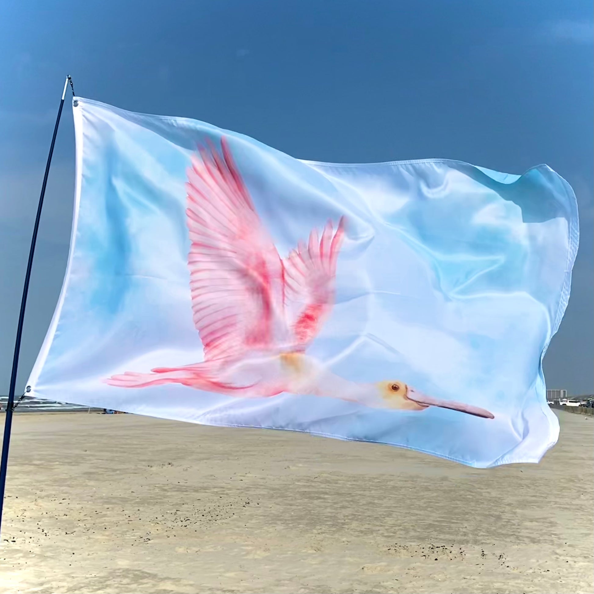 Flag with a pink spoonbill design waving on a beach