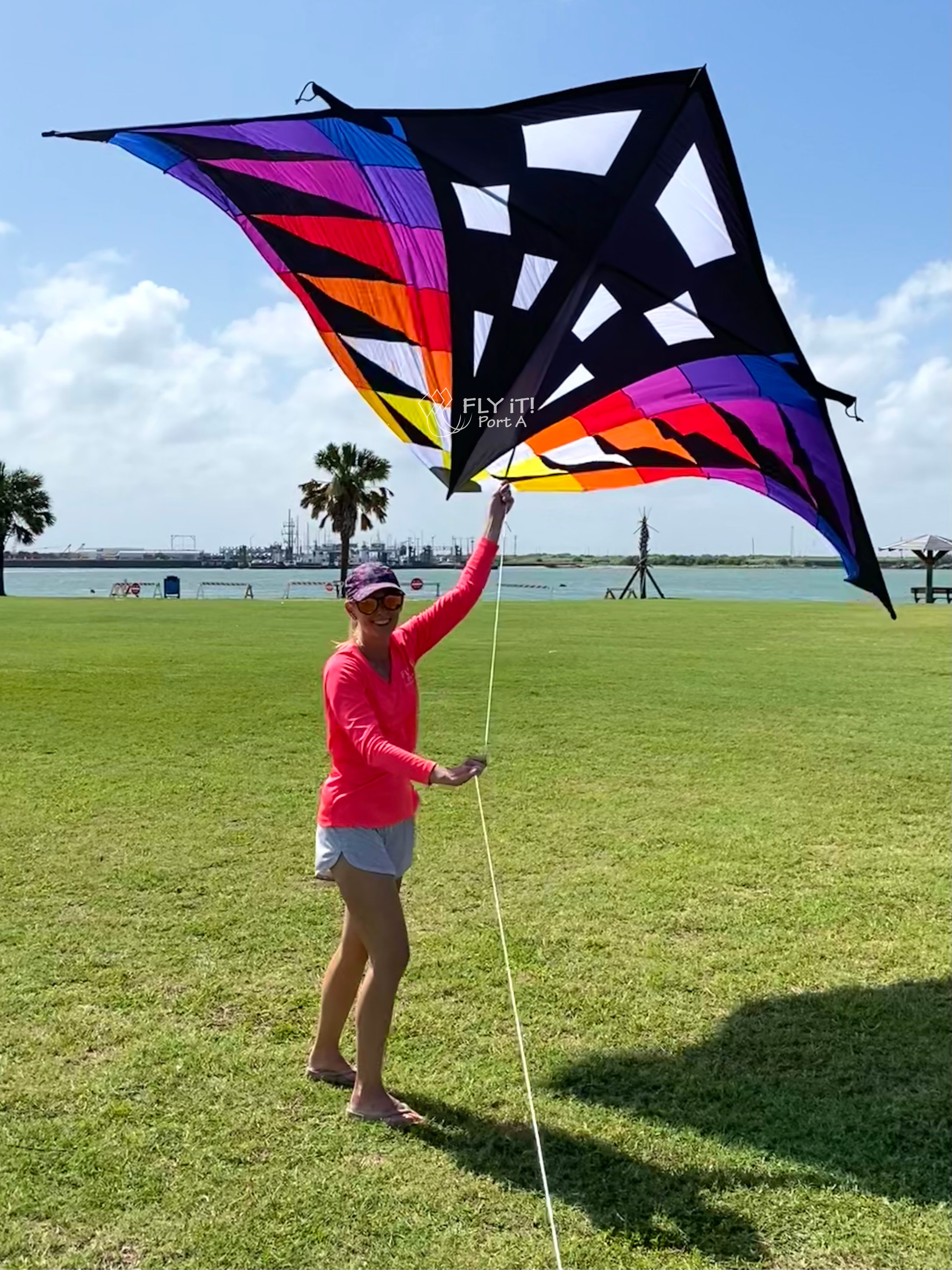 Large Colorful delta kite with colorful against a blue sky. A person in a pink shirt is holding onto the kite line.