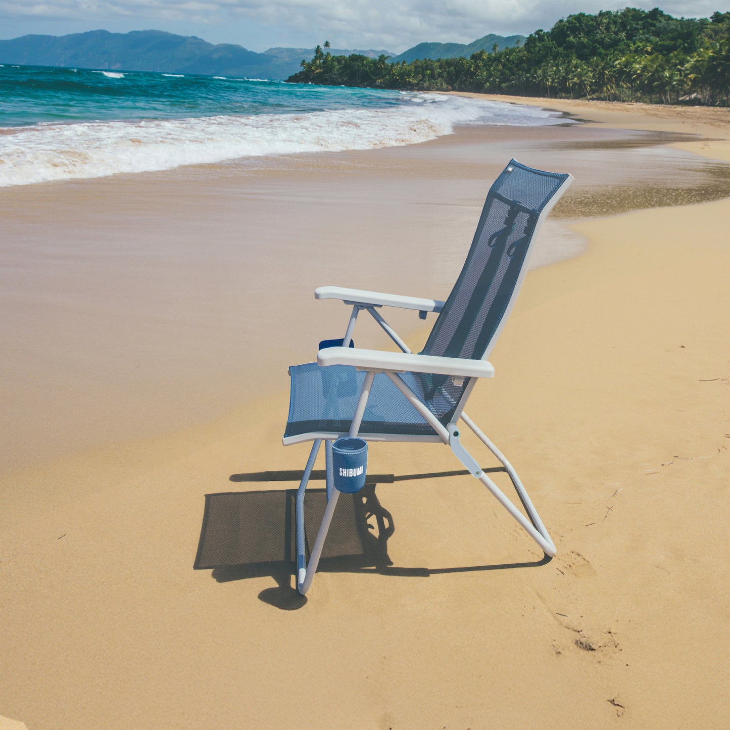 Beach chair on a sandy beach with ocean and mountains in the background