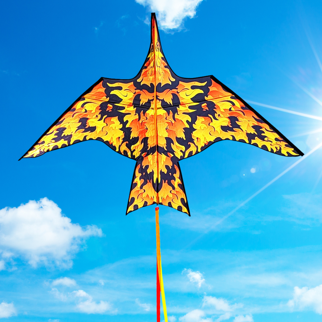 A colorful kite designed in a bird-like shape with a flame pattern in yellow and black, flying against a blue sky with few clouds.