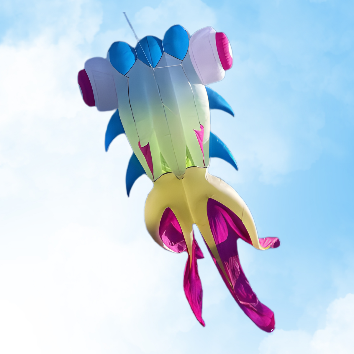 A colorful fish-shaped kite flying against a bright blue sky with light clouds. The kite features a gradient body transitioning from blue to green and yellow, with pink and purple accents on its fins and tail.