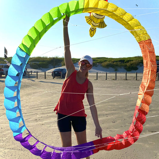 Person holding a large, colorful ring kite on a beach.