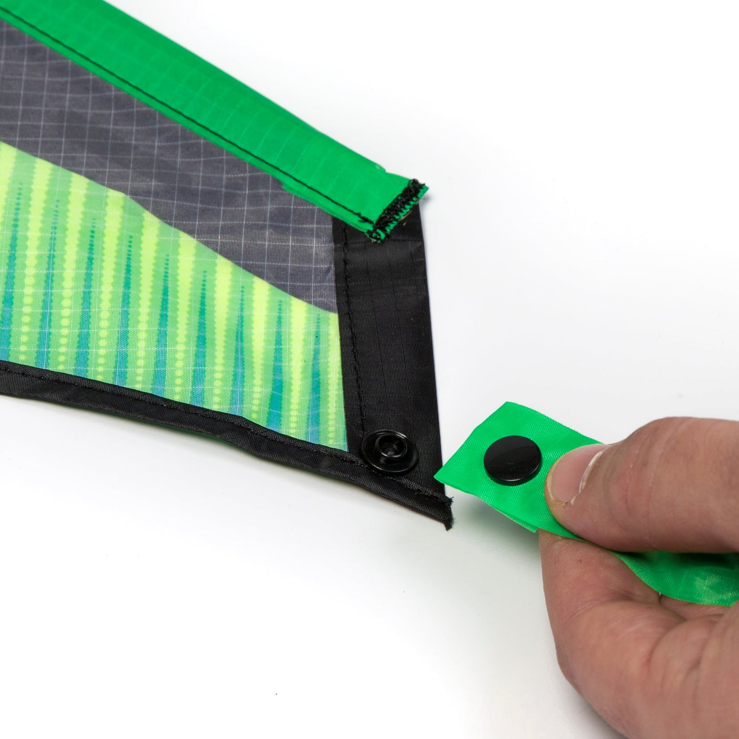 Close up of a hand attaching a Zenith 5 Kite tail with a button on a white background. 