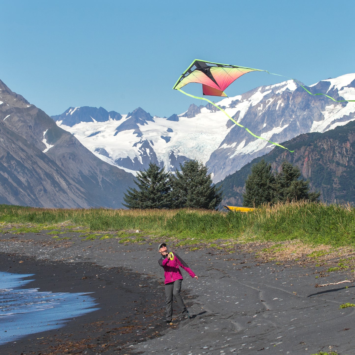 Person flying a colorful kite on a beach with mountains in the background