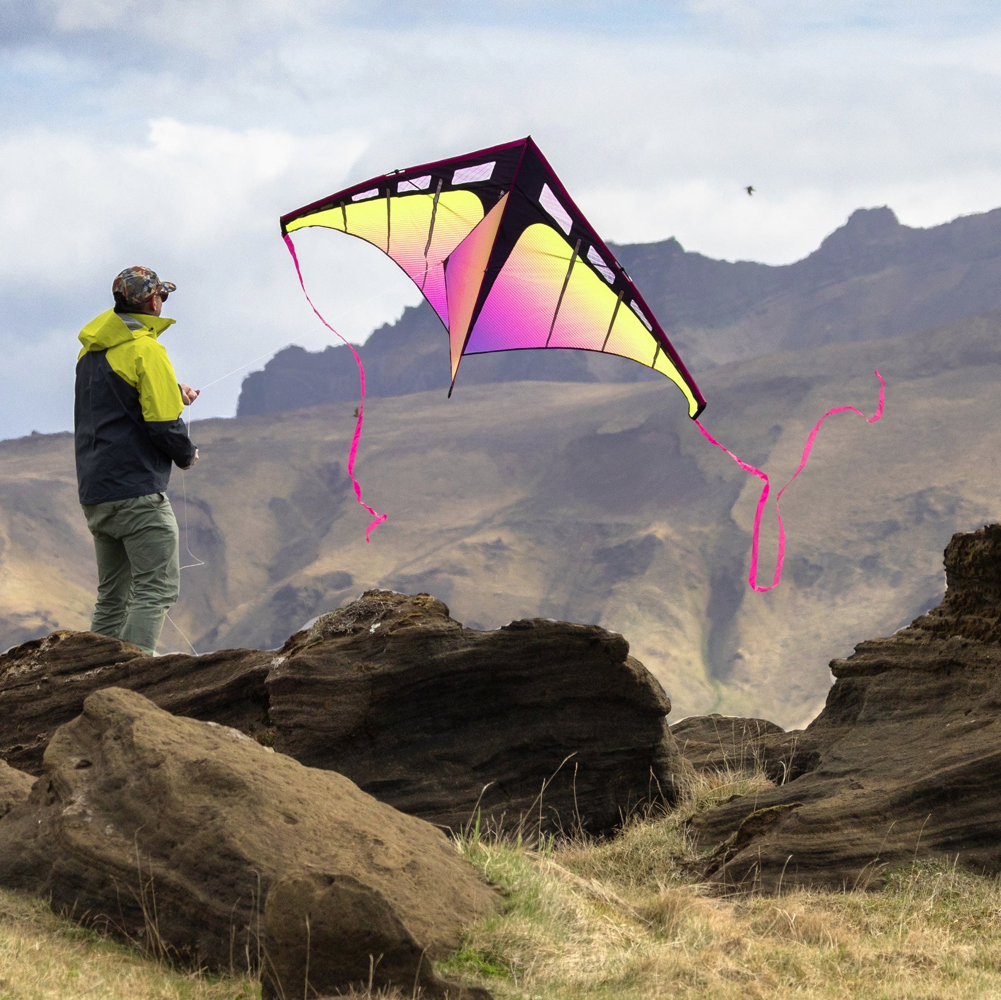 Person flying a colorful kite on a rocky landscape with mountains in the background